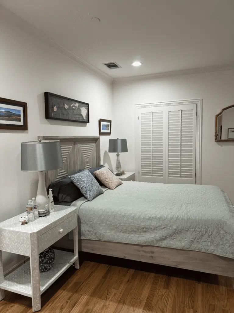 Guest bedroom with sage green bedding, gray wood headboard, matching nightstand lamps and hardwood floors