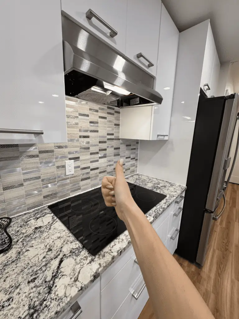 Thumbs up over clean kitchen with black glass cooktop, granite countertops and white cabinets after cleaning