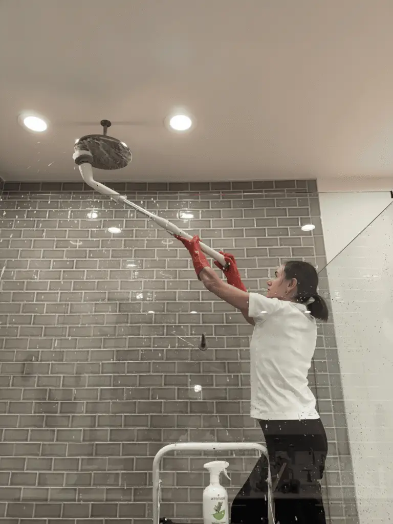 Professional cleaner scrubbing rain shower head with electric brush in tiled bathroom